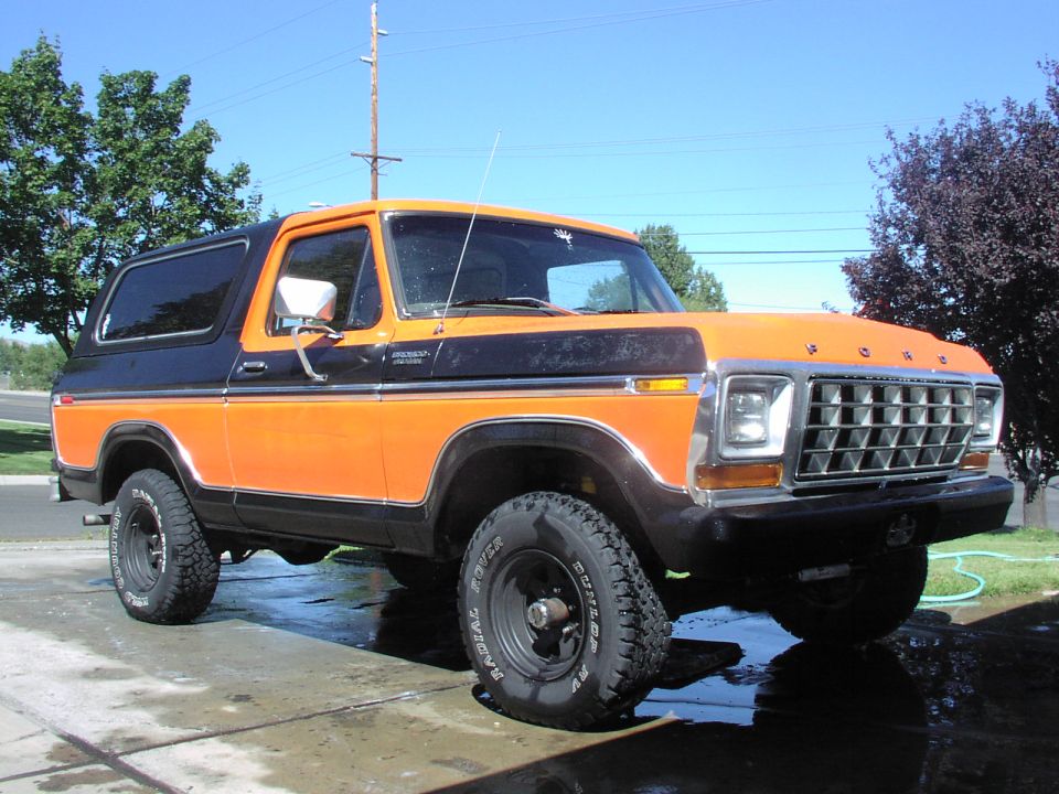 Orange and black 1978 Ford Bronco parked on wet concrete, front 3/4 view