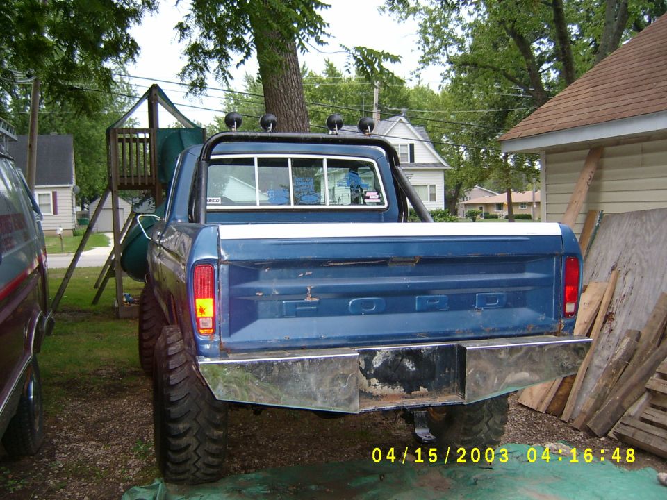 Blue Ford pickup truck rear view, chrome bumper, roll bar, large tires. Some rust on bumper