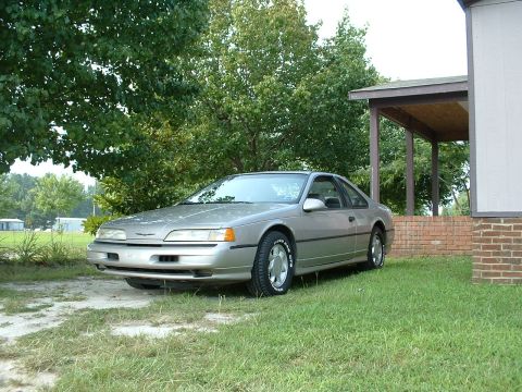 1989 Ford Thunderbird - A silver 1989 Ford Thunderbird is parked on a grassy area next to a house with a covered porch.