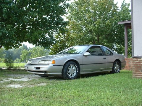 1989 Ford Thunderbird - A silver 1989 Ford Thunderbird coupe is parked on a grassy lawn beside a brick and siding house.