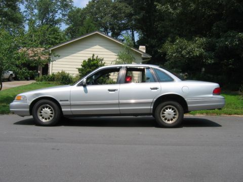 1985 Ford LTD Crown Victoria - A silver sedan is parked on the side of a residential street.