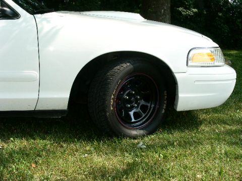 2001 Ford Crown Victoria - A close-up view of the front fender and wheel of a white 2001 Ford Crown Victoria, seen from the side.