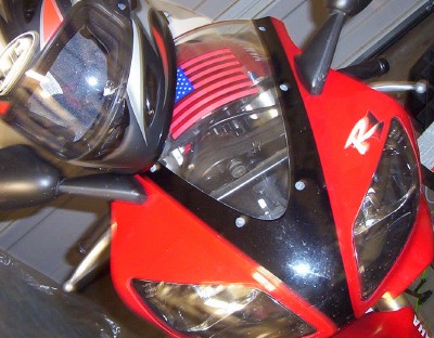 1995 Ford Bronco - A red motorcycle is shown from the front, an American flag sticker and a helmet. The Supermotors.net logo is visible at the bottom.