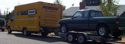 1995 Ford Bronco - A Penske box truck is seen towing a pickup truck on a trailer.