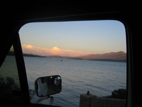 1990 Ford Bronco - wide lake with distant hills glows at sunset, seen through a vehicle window with the side mirror in the foreground.