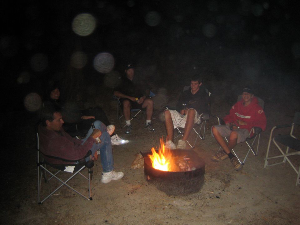 Group of people seated in camp chairs around a glowing campfire at night