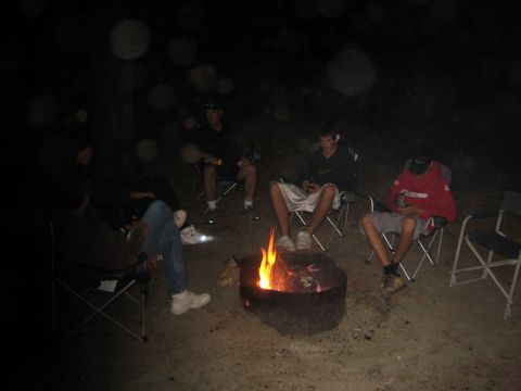 1990 Ford Bronco - group sits in folding chairs around a fire pit at night, faces lit by the flames, one person wearing a bright red jacket.