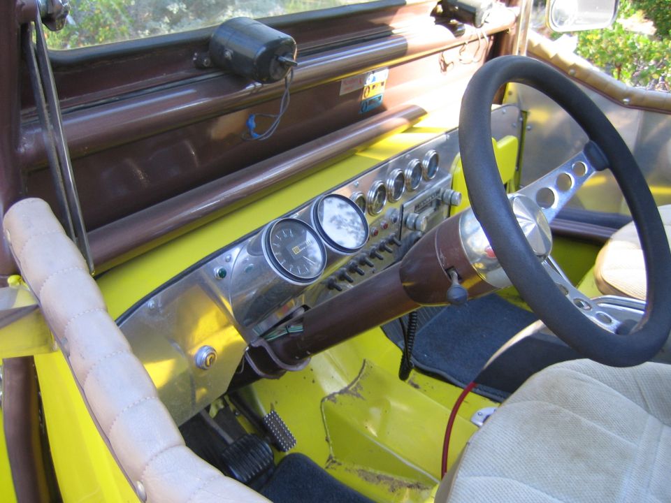 Dashboard and steering wheel inside an open yellow Jeep with aftermarket gauges