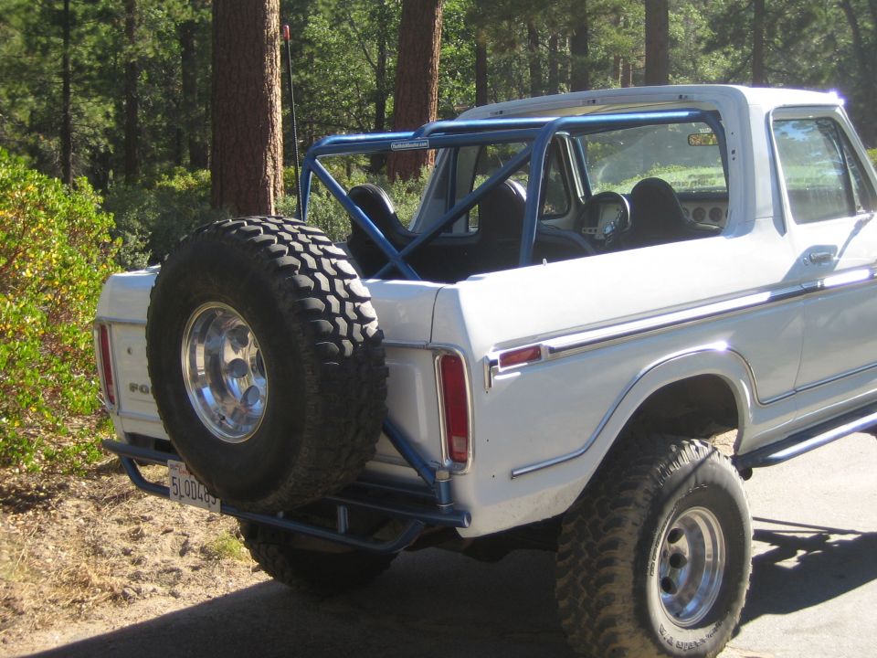 Rear three-quarter of a white Ford Bronco with blue roll cage and rear spare tire