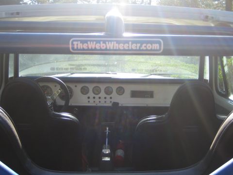1990 Ford Bronco - Looking forward from the back of an open vehicle: black bucket seats, a metal dash with round gauges, and a TheWebWheeler.com windshield de…
