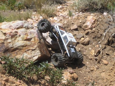 1990 Ford Bronco - small white off-road crawler with oversized tires climbs at a steep angle over rocks and dirt.