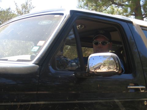 1990 Ford Bronco - man wearing sunglasses and a cap sits in the driver seat of a dark Ford SUV with the window down.