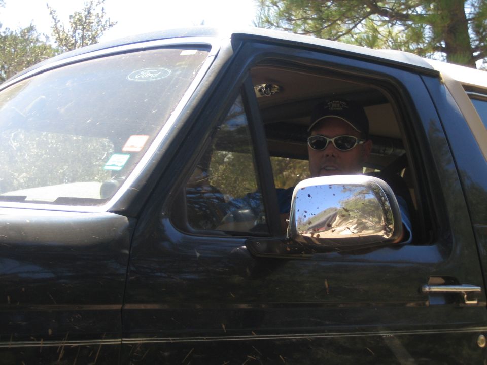 Man in sunglasses and cap seated in the driver seat of a dark Ford SUV