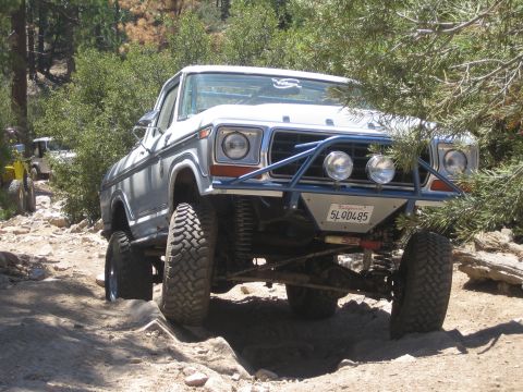 1990 Ford Bronco - white vintage Ford pickup with a tube bumper and round driving lights climbs a rocky off-road trail.