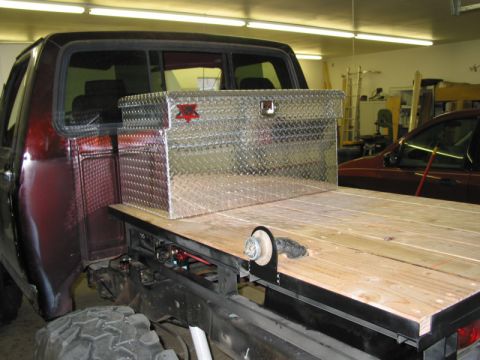 1981 Ford Bronco - A red pickup truck bed is shown with a wooden deck and a diamond plate toolbox, with another vehicle visible in the background.