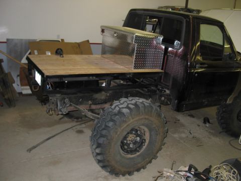 1981 Ford Bronco - Pickup truck modified with a flatbed and toolbox, large off-road tires.