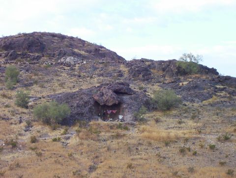 1995 Ford Bronco - A dry, rocky desert scene with sparse vegetation and a small cave in the hillside.
