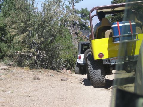 1990 Ford Bronco - Rear view of a yellow open Jeep carrying a cooler with a white Jeep following on a dusty dirt trail.