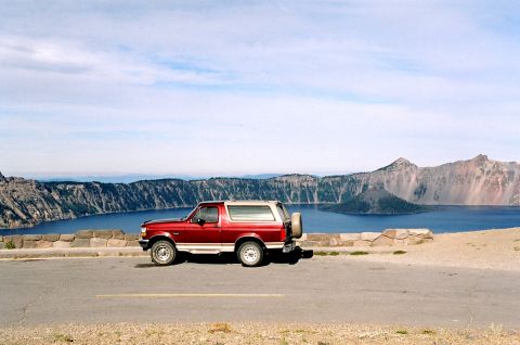 1979 Ford Bronco - A red SUV is parked on the side of the road with a scenic view of Crater Lake and the surrounding mountains.