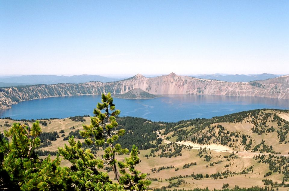 View of Crater Lake with Wizard Island and surrounding mountains under a clear blue sky