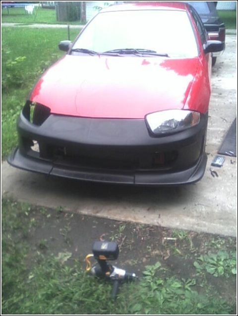 2005 Chevrolet Cavalier - Front view of a red car with a modified black bumper and front lip, parked outdoors.
