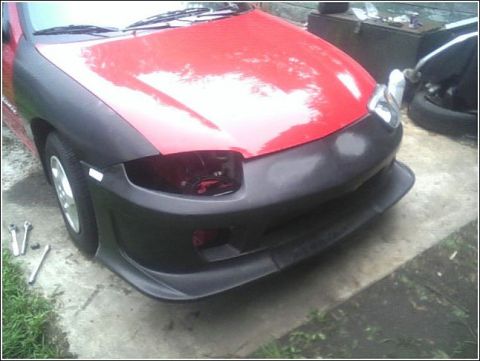 2005 Chevrolet Cavalier - The front of a red car is shown with unpainted black fender flares and a new bumper cover installed.