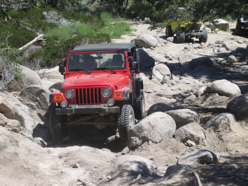 Red Jeep Wrangler descending a boulder-strewn rock trail