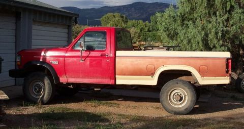 1990 Ford Bronco - Side view of a red pickup truck with a two-tone bed, parked outdoors.