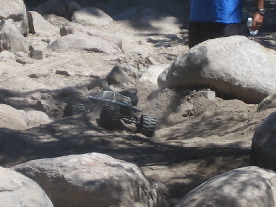 Small silver RC rock-crawler truck on big tires among real boulders