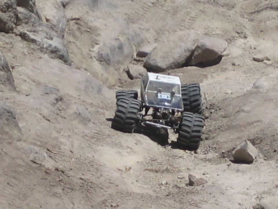 Silver RC monster-truck rock crawler climbing a dirt embankment