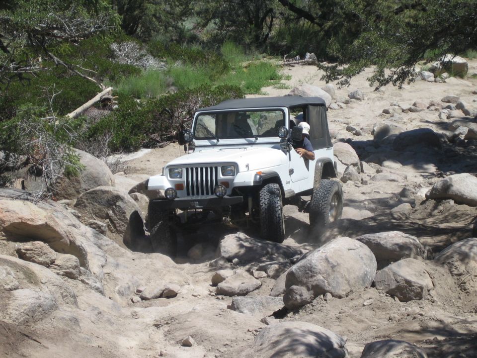 White Jeep Wrangler YJ crawling over rocks on a sandy desert trail