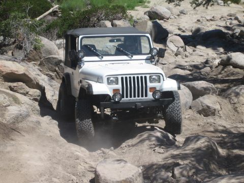 1990 Ford Bronco - white Jeep Wrangler with square headlights and a windshield light bar crawls forward over large boulders.