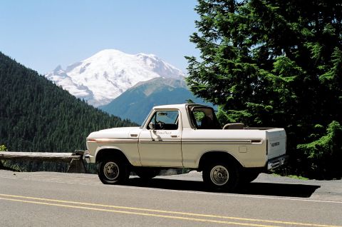 1979 Ford Bronco - A white 1978 Ford Bronco is parked on the side of a mountain road with a snow-capped mountain in the background.
