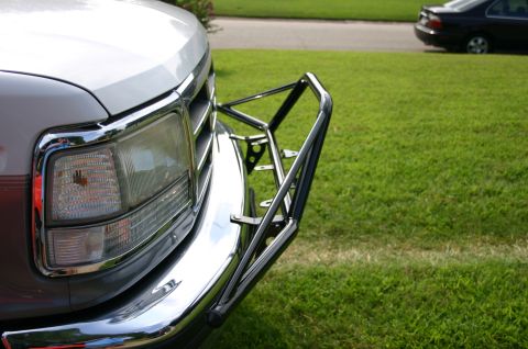 1994 Ford Bronco - Close-up of the front driver-side corner of a white Ford truck/SUV, showing the chrome-trimmed headlight, chrome bumper, and a newly instal…