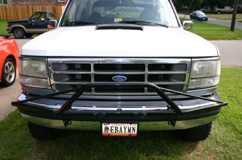 1994 Ford Bronco - Head-on view of a white Ford Bronco's nose showing a black tubular pre-runner-style guard mounted over the chrome front bumper, chrome gril…