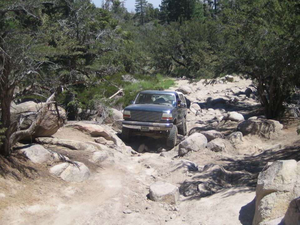 Dark green lifted SUV crawling a rocky trail between boulders and trees