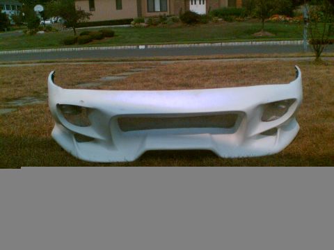 1997 Ford Probe - Aftermarket fiberglass front bumper cover in white primer standing upright on a residential lawn, showing its wide center mouth opening, me…