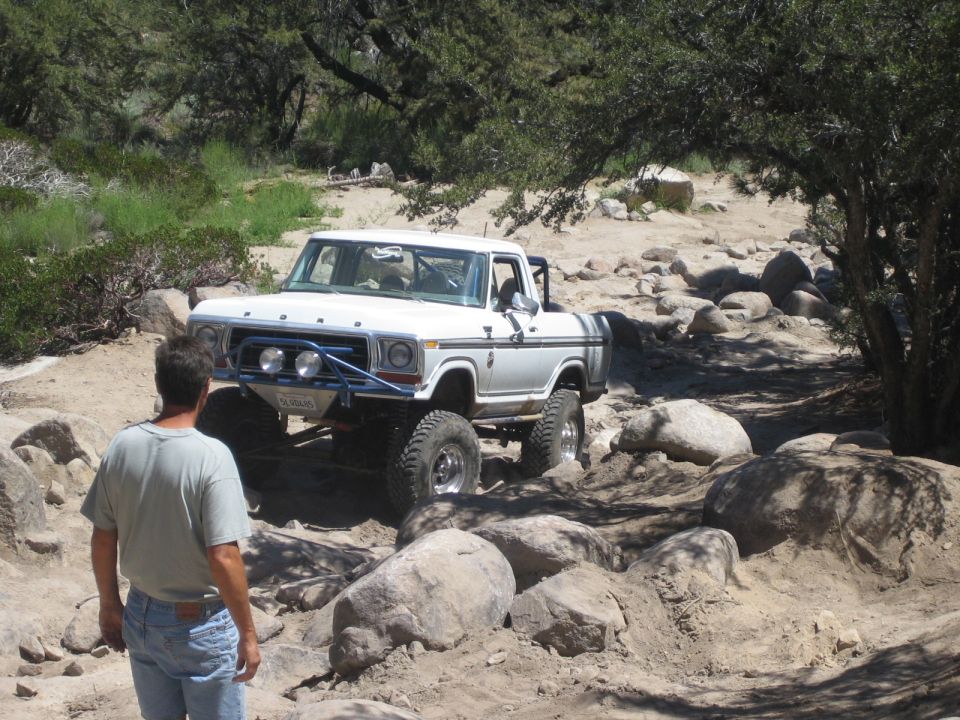 White Ford pickup with rollbar parked on a dry rocky creek bed, man watching