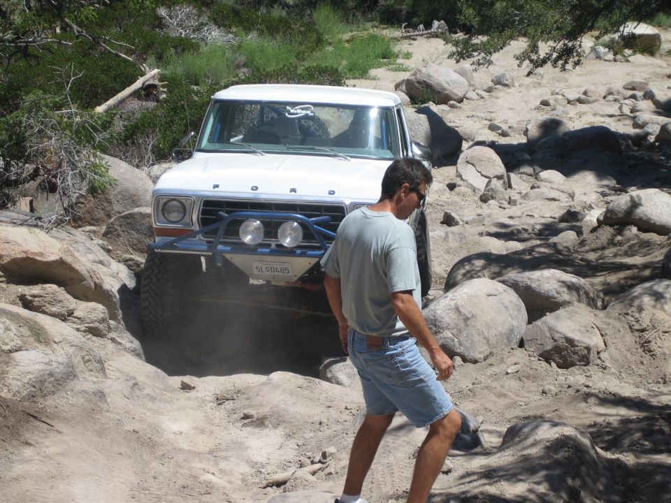 Man in shorts walking past a white Ford truck crawling over rocks