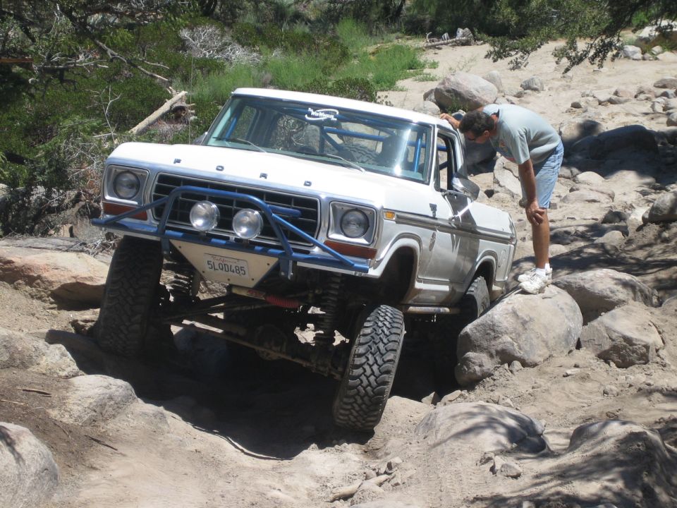 White Ford truck on rocks while a man bends to inspect the front wheel