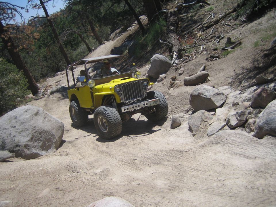 Yellow flat-fender Jeep with headlights on descending a dusty hill