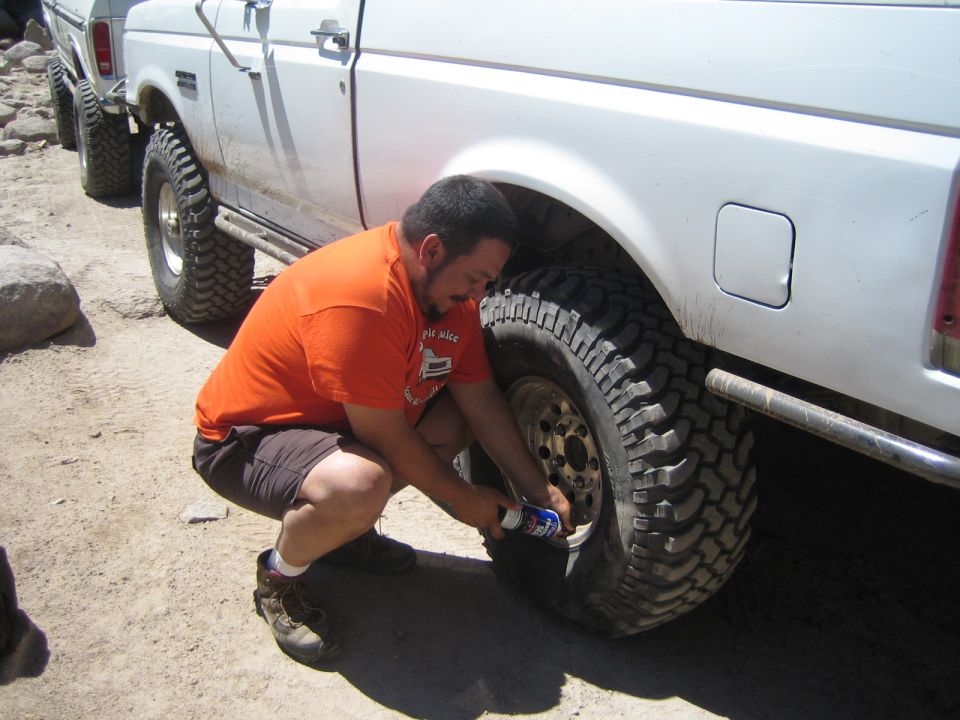 Man in orange shirt crouching to air down the rear tire of a white truck