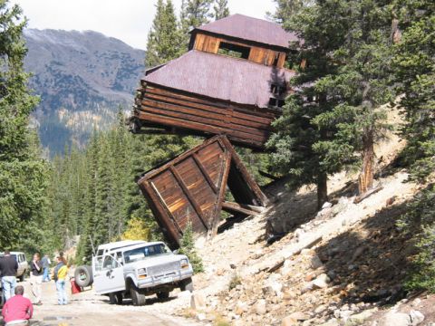 1981 Ford Bronco - A white Ford F-Series truck navigates a rough mountain road beside a precarious, old wooden building.