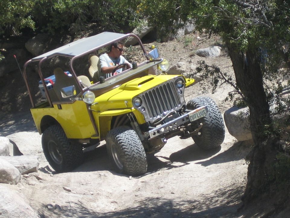 Driver in a yellow flat-fender Jeep with rollbar crawling over rocks