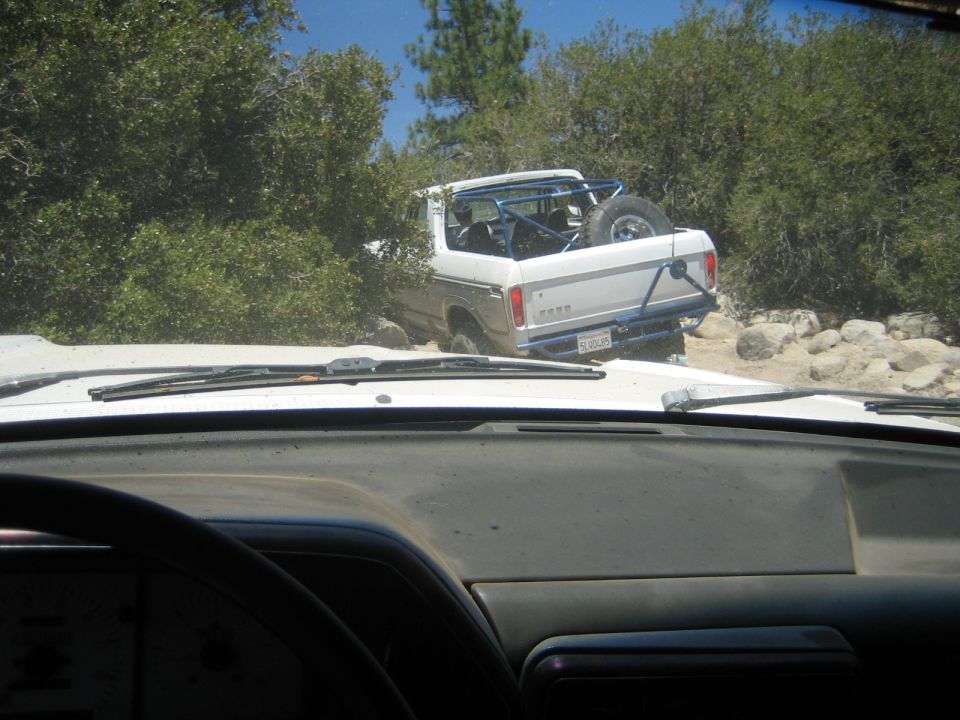 View through dusty windshield of white pickup with roll bar climbing rocky off-road trail