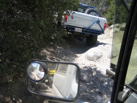 1990 Ford Bronco - lifted white Ford pickup with a blue tube bumper climbs a rocky trail, reflected alongside in the photographer vehicle's side mirror.