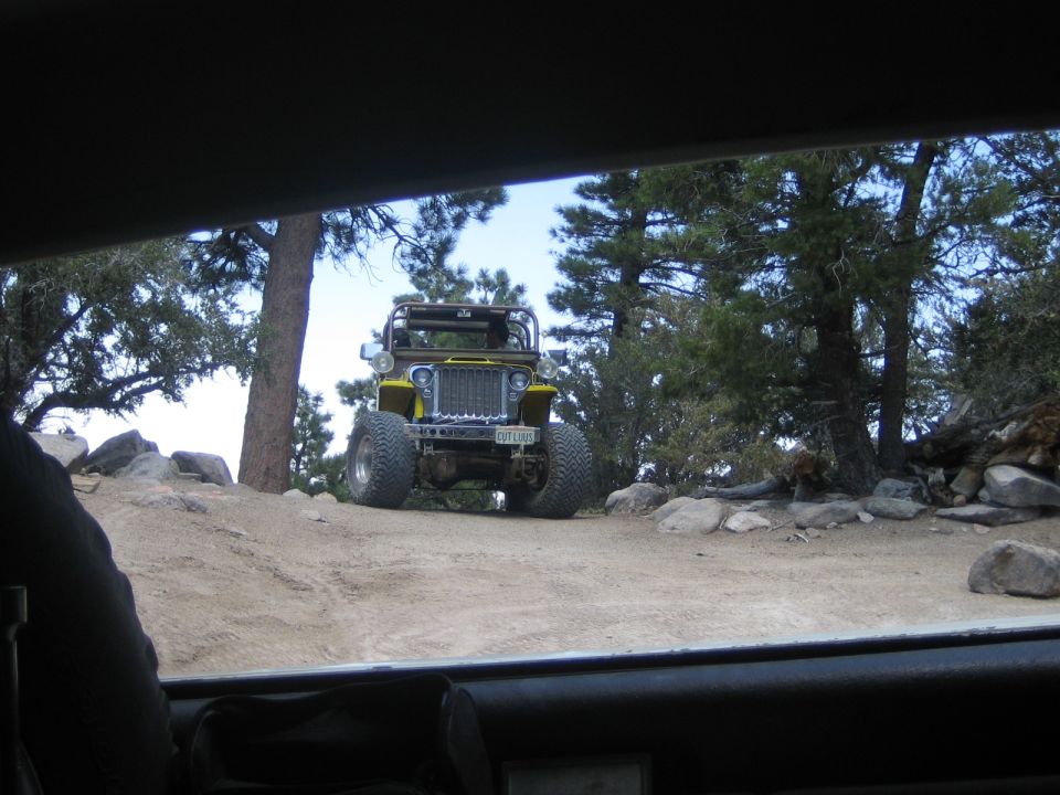 Yellow open-top Jeep on a dirt trail viewed through a vehicle windshield