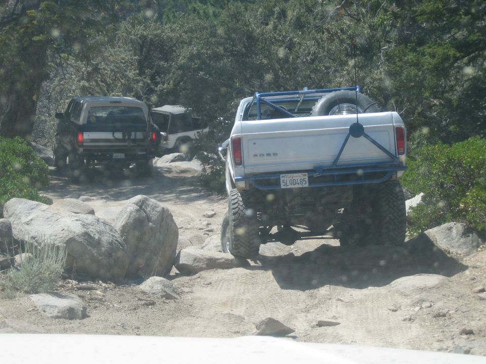 Rear of a lifted white Ford pickup and dark SUVs on a rocky trail