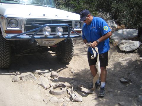 1990 Ford Bronco - man in a blue shirt and ball cap coils a recovery tow strap in front of a white Ford truck with a blue tube bumper and round lights.