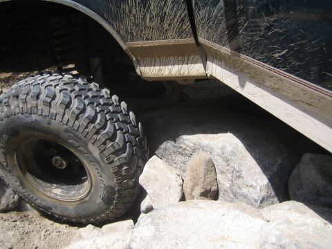 1990 Ford Bronco - large knobby mud-terrain tire on a lifted truck flexes against jagged granite boulders on a rocky trail.